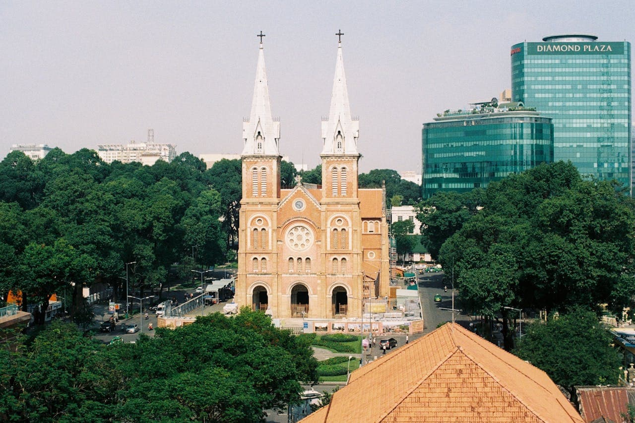Aerial view of the Notre-Dame Cathedral Basilica of Saigon in Ho Chi Minh City, Vietnam, with twin bell towers and surrounding modern buildings and greenery.