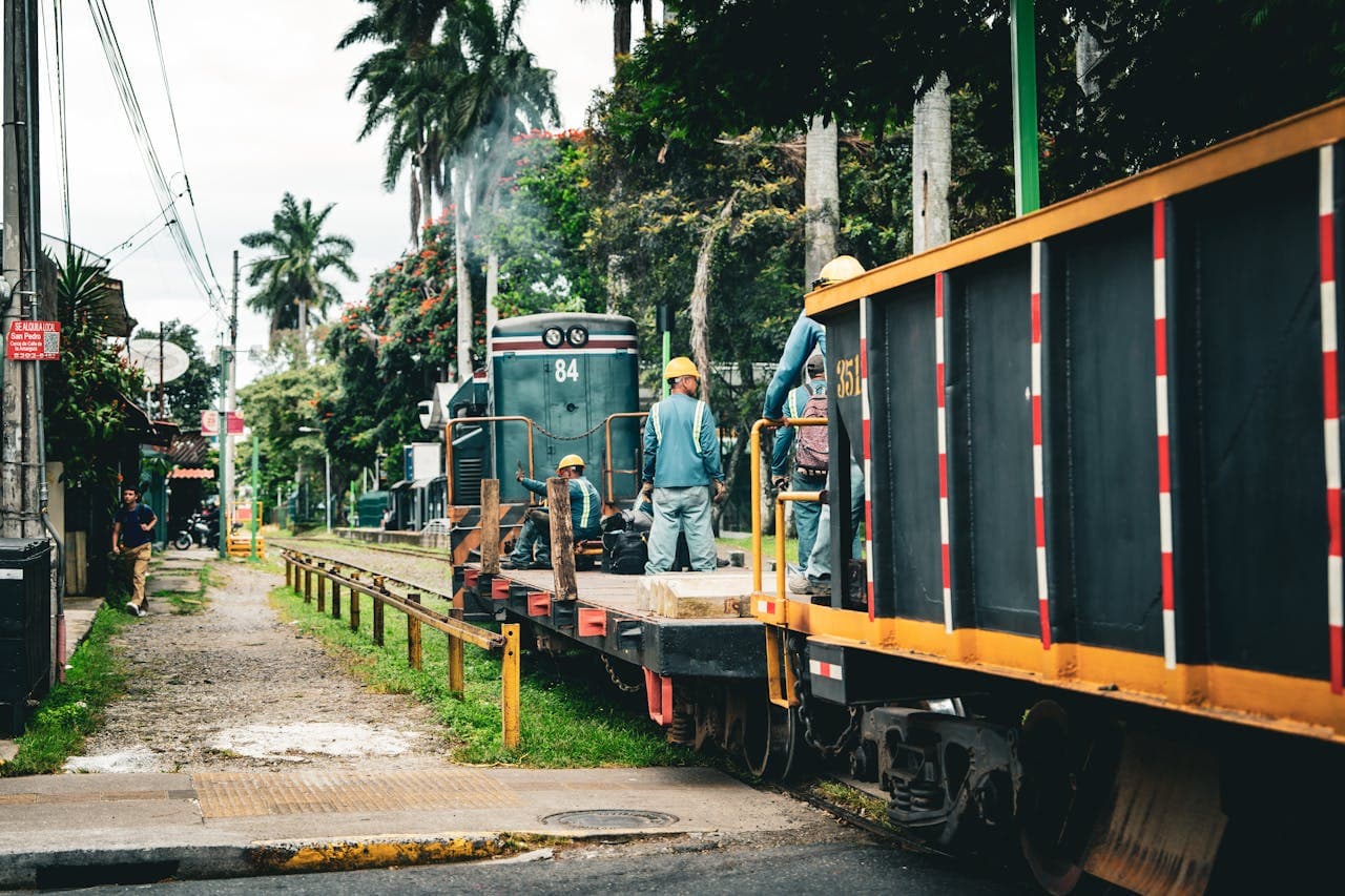 Railway maintenance crew working on train tracks in a tropical urban area with palm trees and greenery