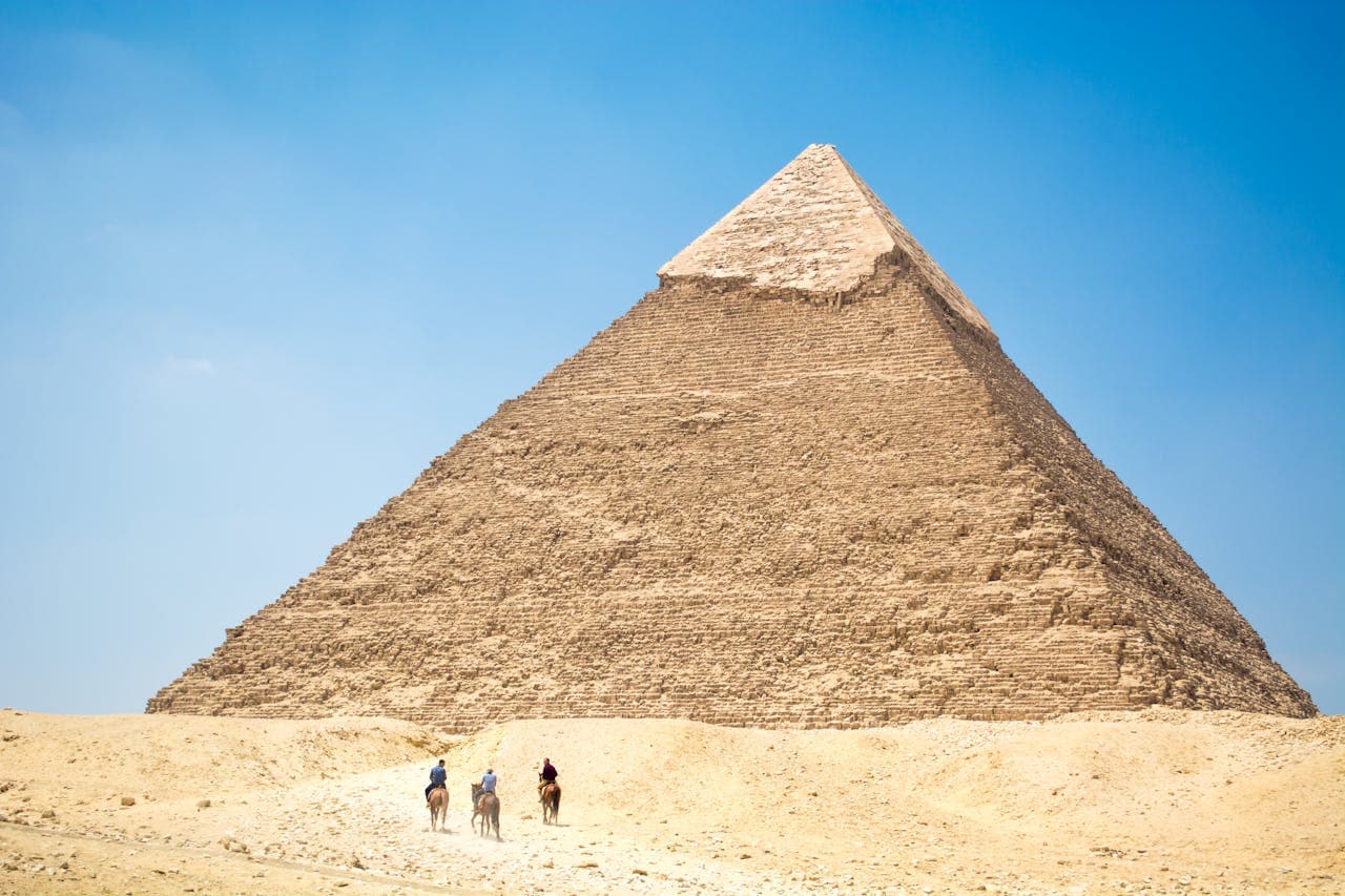 Tourists riding camels toward the Great Pyramid of Giza under a clear blue sky in Cairo’s desert