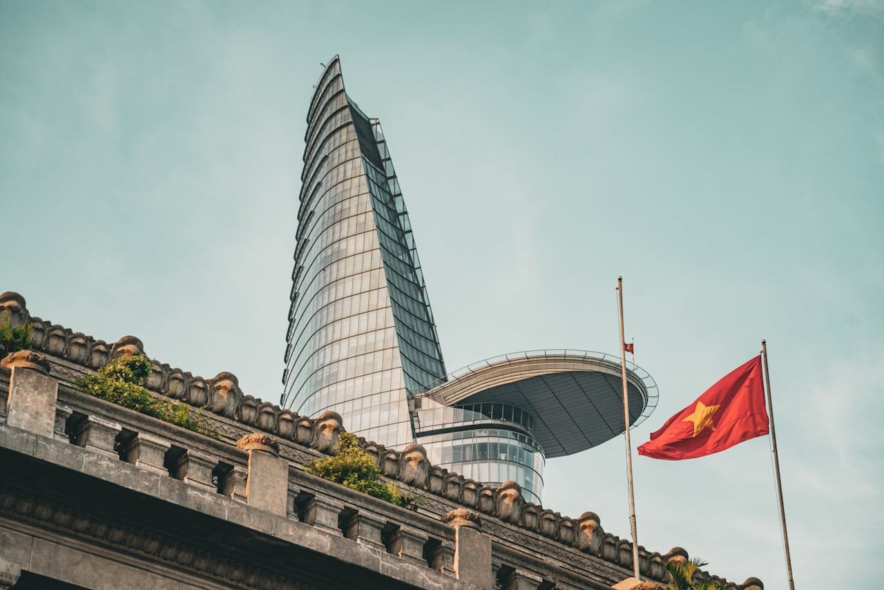 Modern skyline view of Bitexco Financial Tower in Ho Chi Minh City, Vietnam, with Vietnamese flags and classic architecture in the foreground