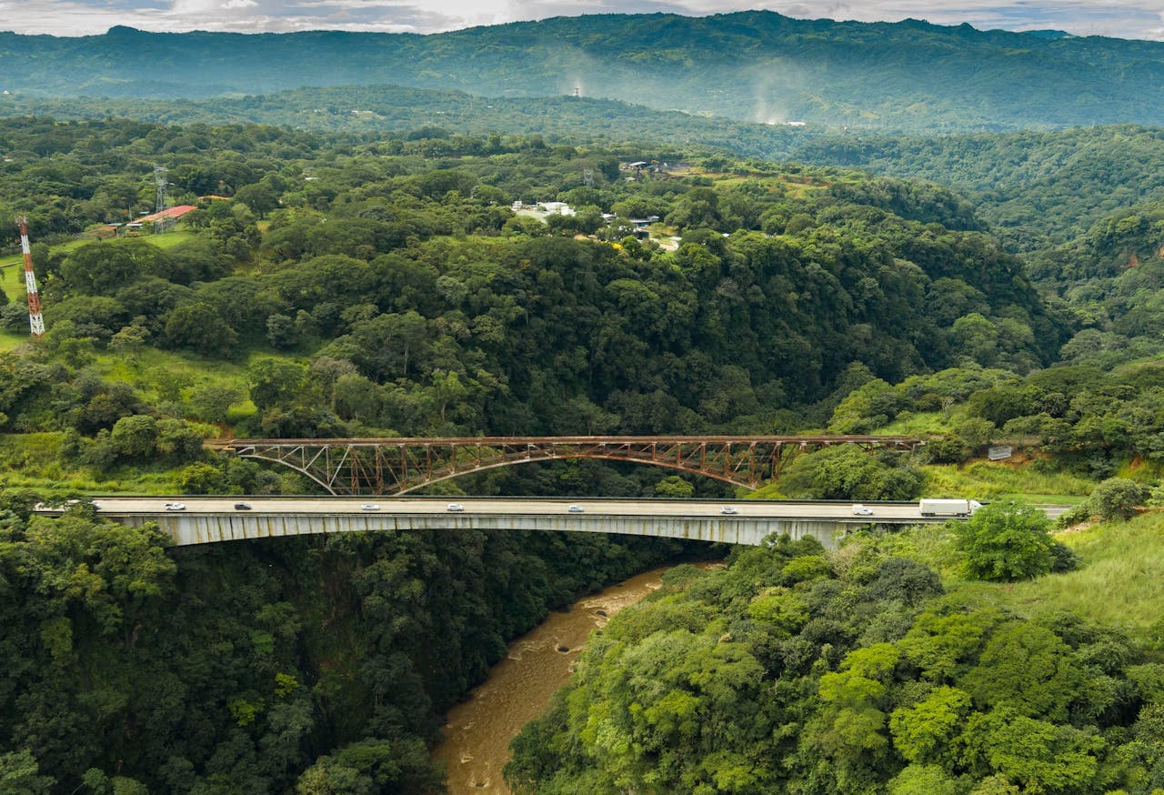 Aerial view of two bridges spanning a lush green canyon with dense forest and mountains in the background, highlighting Costa Rica’s scenic natural landscapes and infrastructure.