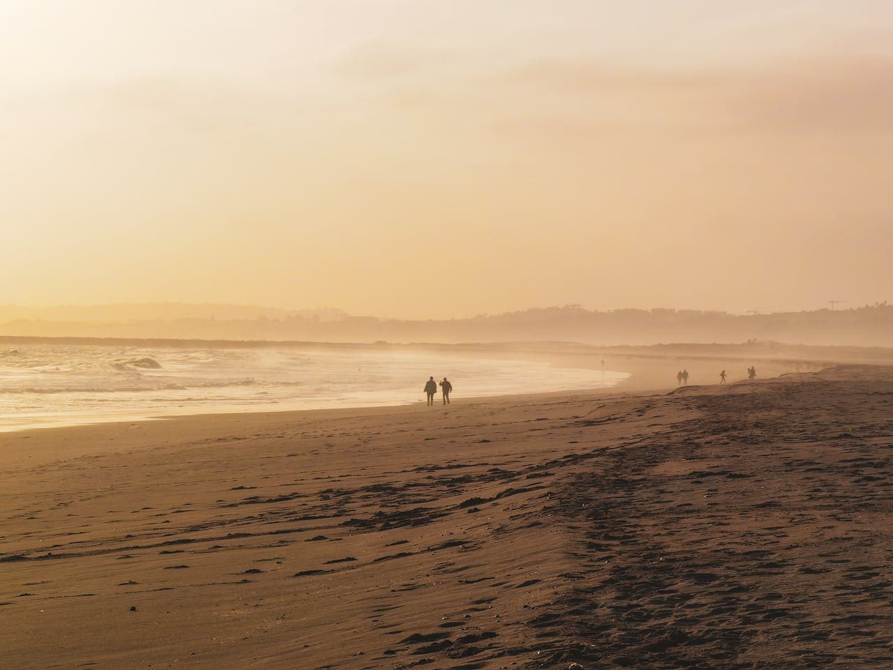 A tranquil beach at sunset with a golden sky, gentle waves, and a few people walking along the shoreline, creating a peaceful and serene atmosphere.