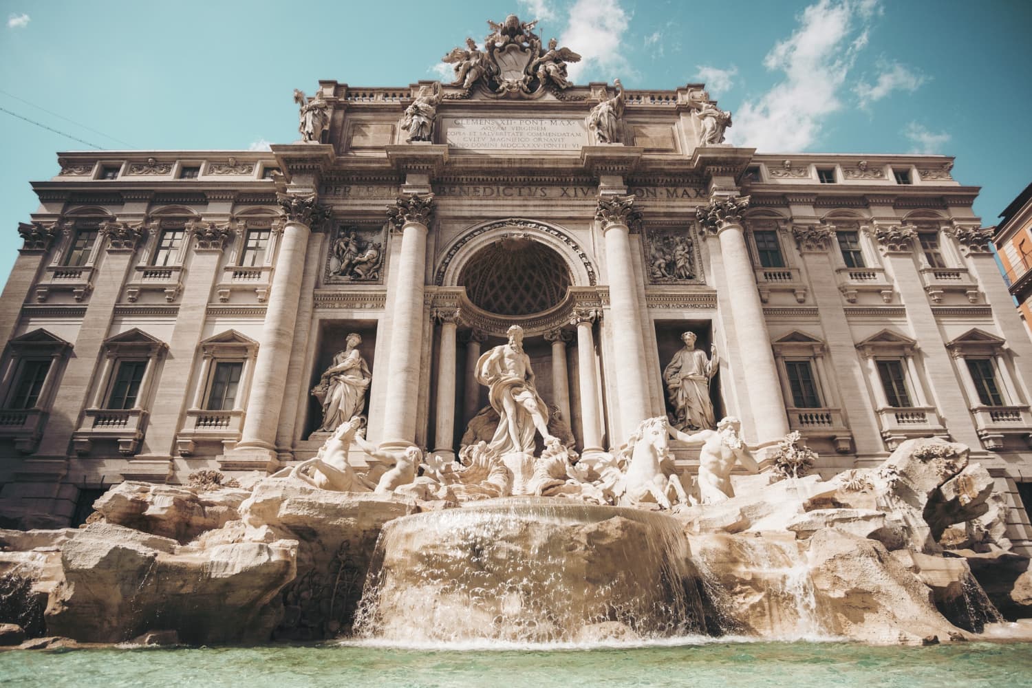 Trevi Fountain in Rome, Italy, featuring Baroque architecture with ornate statues, cascading water, and a clear blue sky in the background.