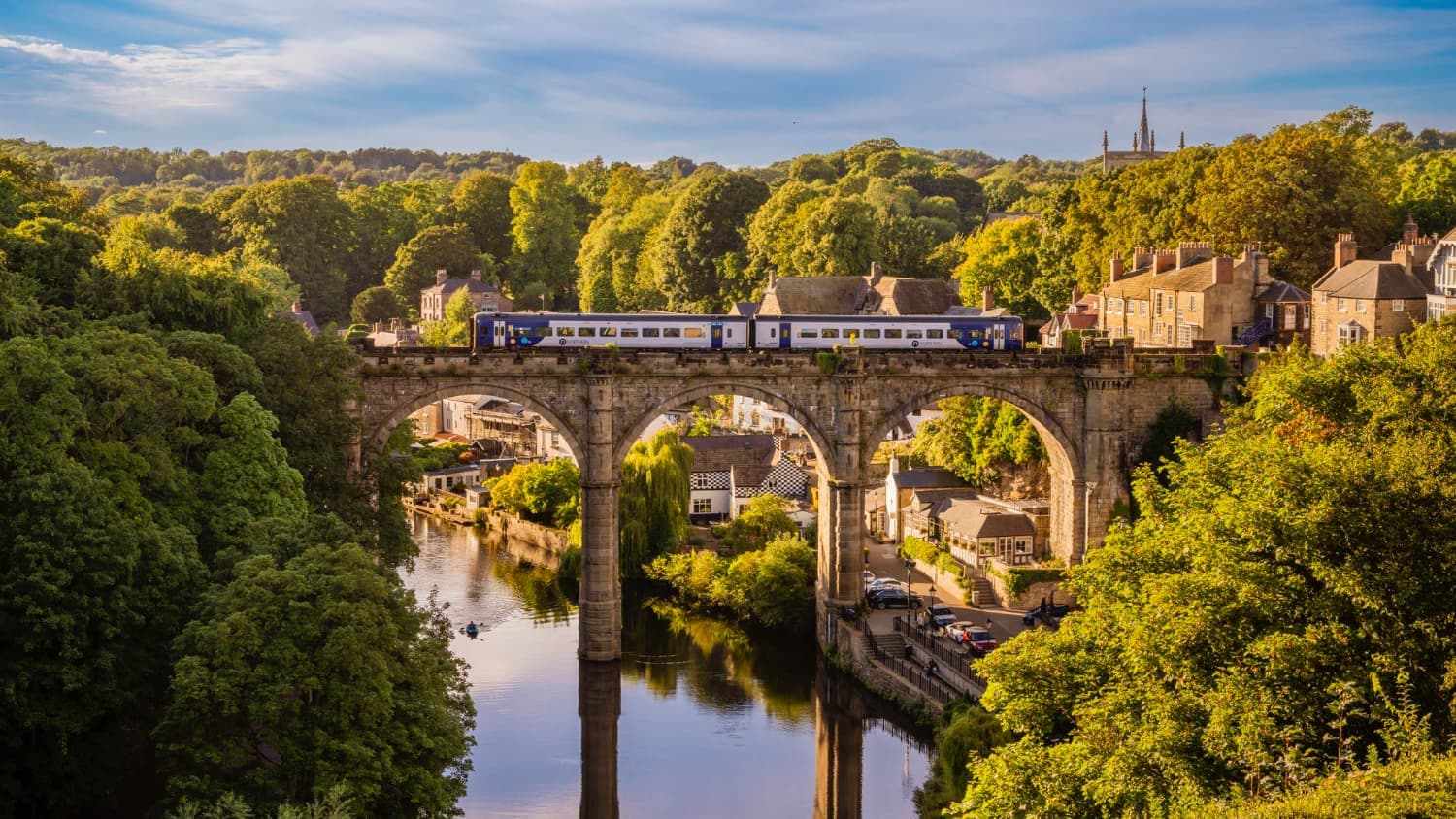 Scenic train crossing historic stone viaduct in rural England during golden hour, showcasing sustainable rail travel through the British countryside in 2025