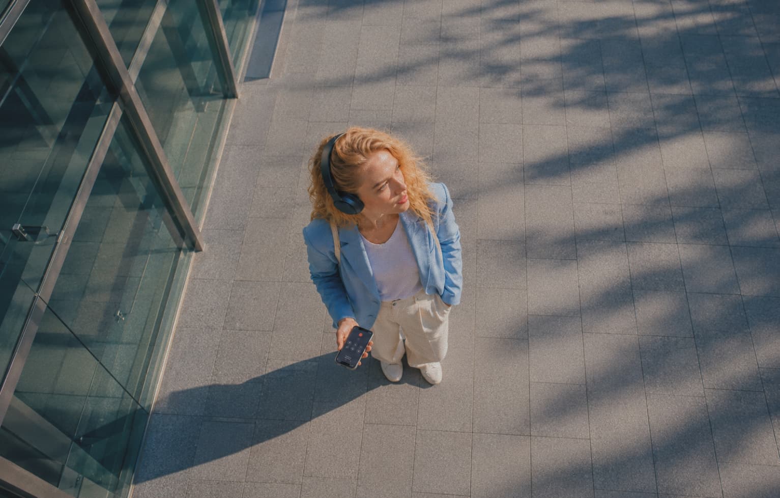 Woman wearing headphones holding her phone outside an office building