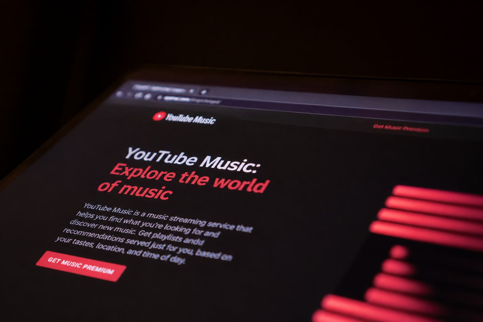 Angled view of a laptop screen displaying the YouTube Music homepage with the tagline "Explore the world of music" on a dark background.
