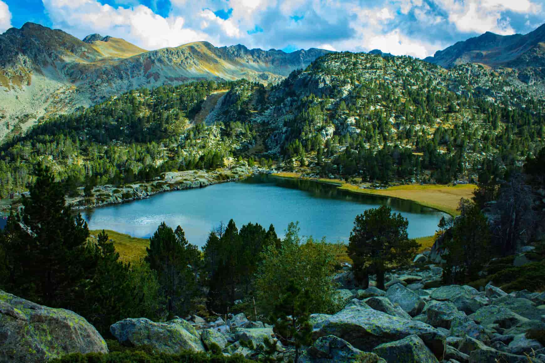 Mountain lake surrounded by rocky slopes and dense forests under a partly cloudy sky.