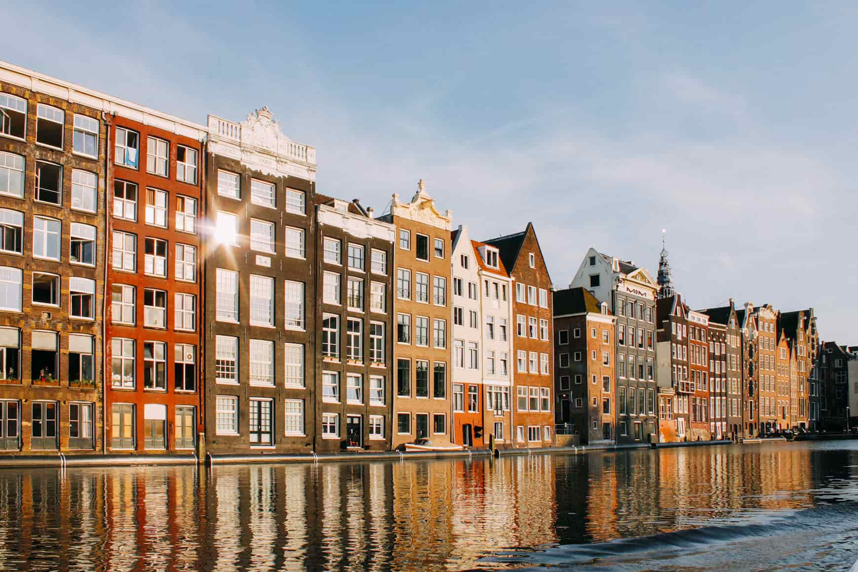 Row of colorful canal houses reflecting in the water under a clear blue sky.
