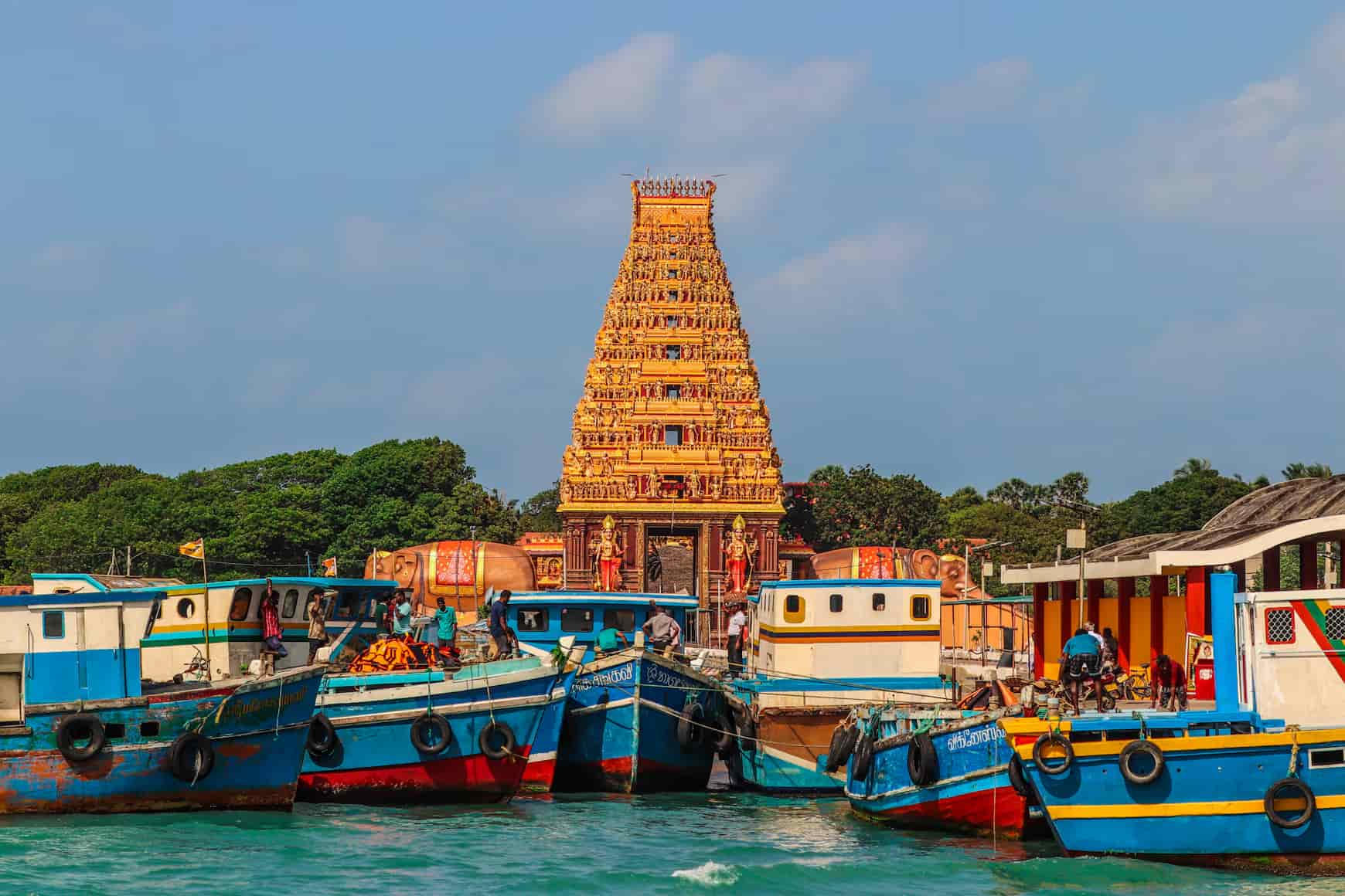 Colorful boats docked near a golden, intricately designed temple tower under a clear blue sky.