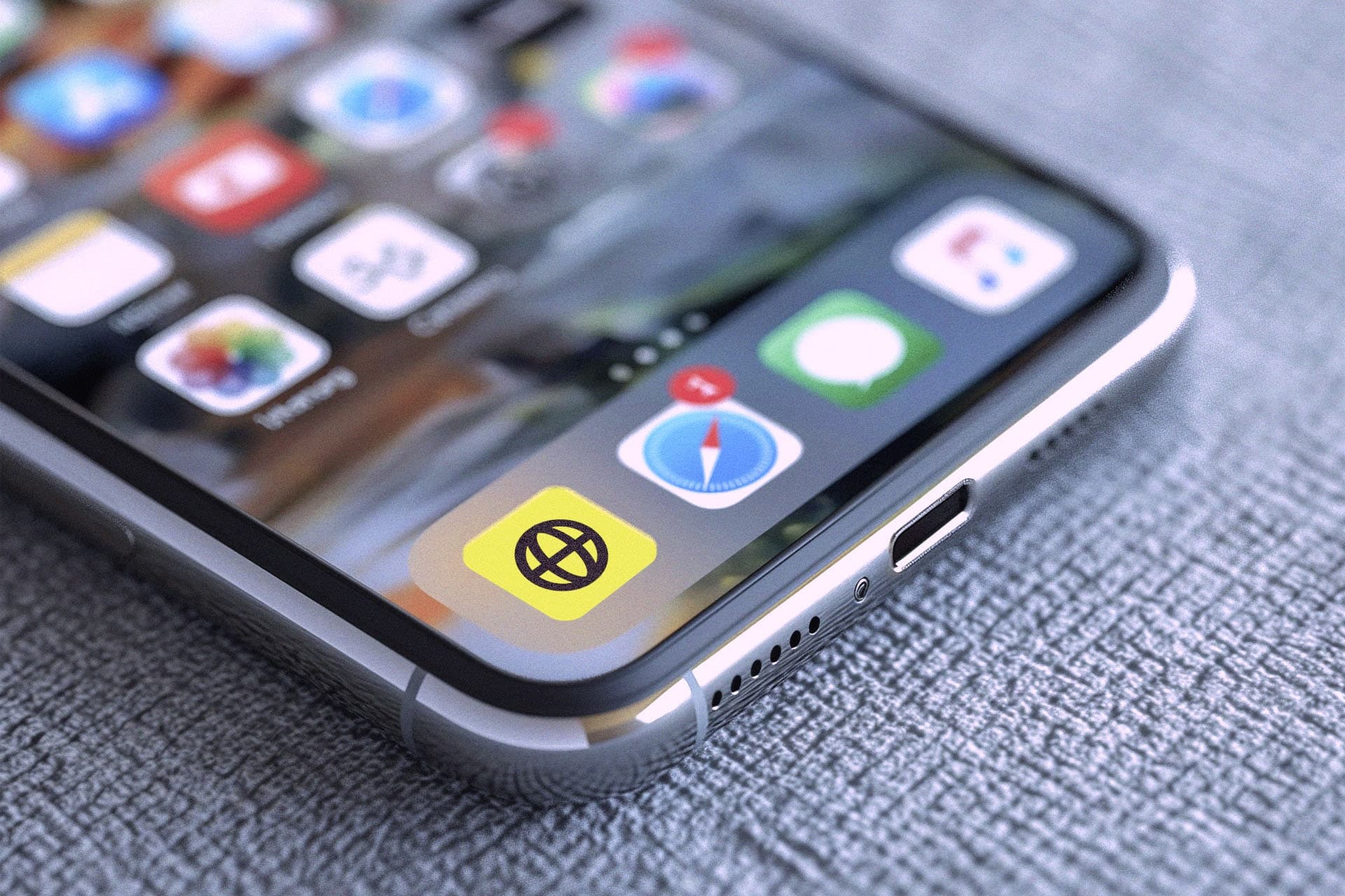 Close-up of a smartphone on a textured surface, displaying various app icons on its screen.