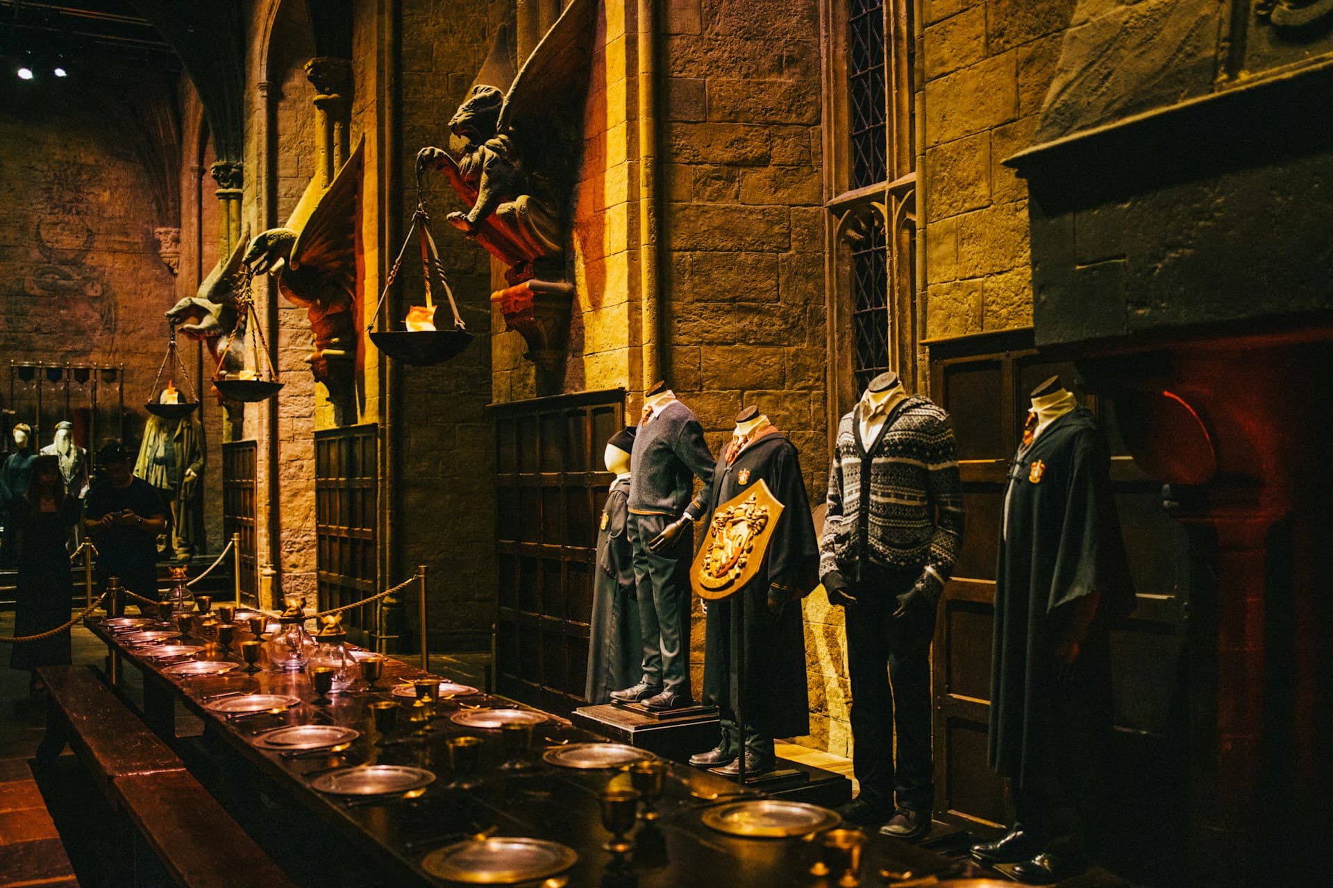 Great Hall exhibit: long banquet table with plates and goblets, cloaked uniforms on mannequins against stone walls.
