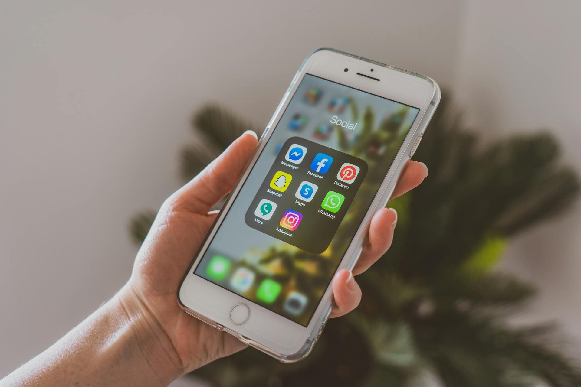 Hand holding a smartphone displaying social media app icons, including Facebook, Twitter, Instagram, and Snapchat, with a blurred background.