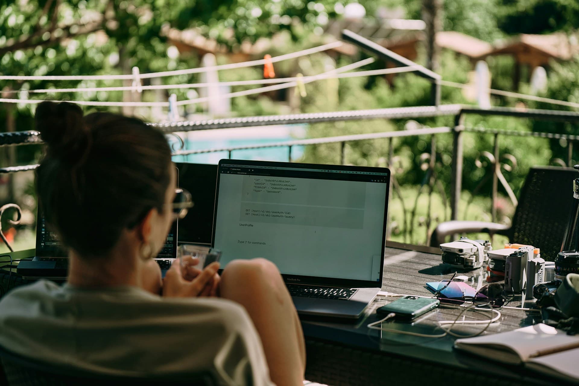 Person working on a laptop outdoors, surrounded by various gadgets, with a garden in the background.