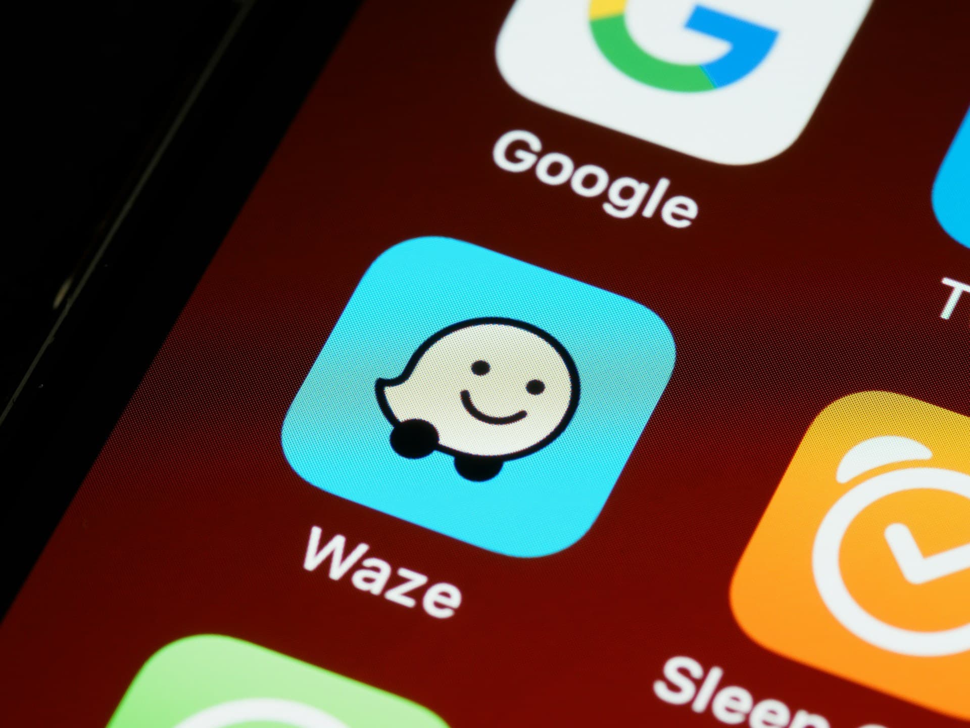 Close-up of smartphone screen showing the Waze app icon, featuring a smiling speech bubble character, alongside other app icons.