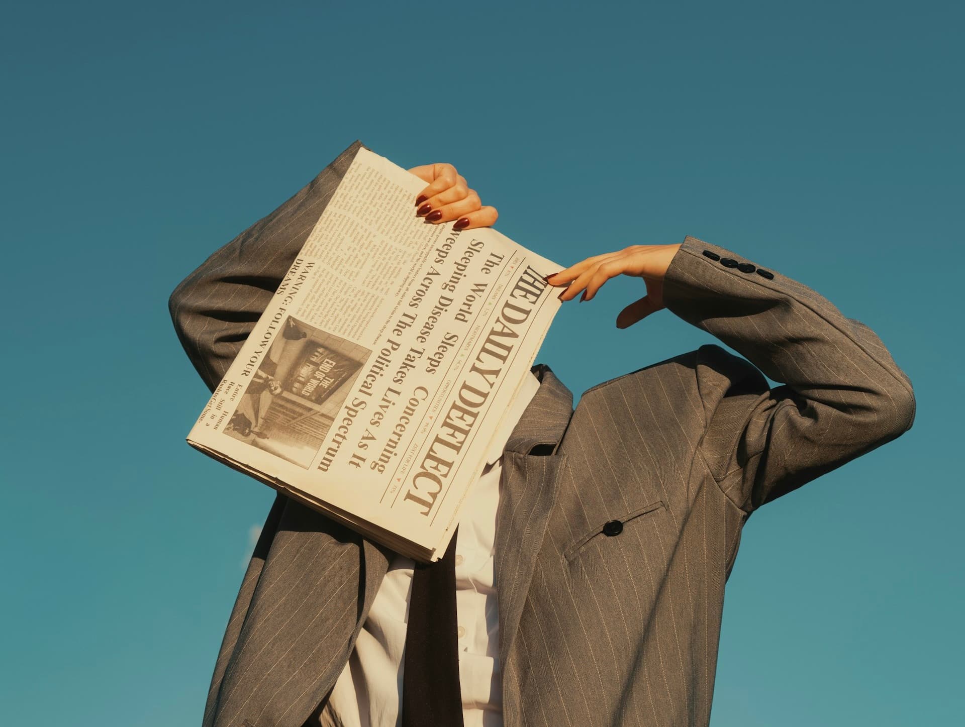 Person in a grey pinstripe suit hiding their face behind a newspaper against a blue sky, illustrating anonymous calling, hidden identity, and private number privacy in Belgium.