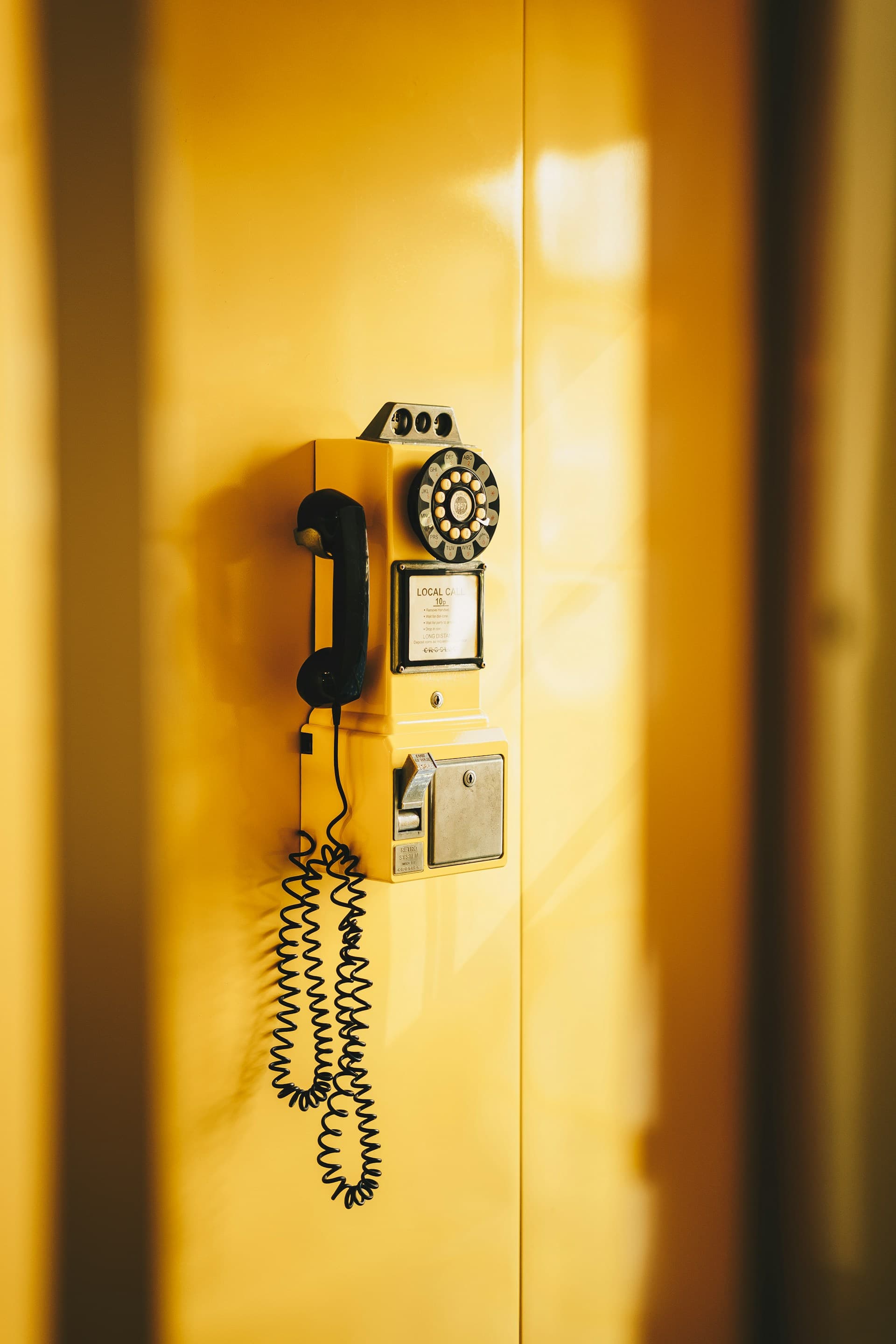 Vintage rotary payphone mounted on a yellow wall