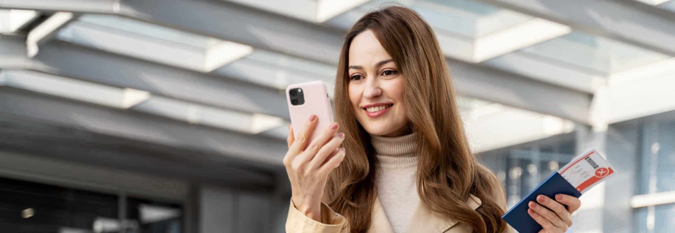 Traveler smiling at her phone while holding a passport and boarding pass