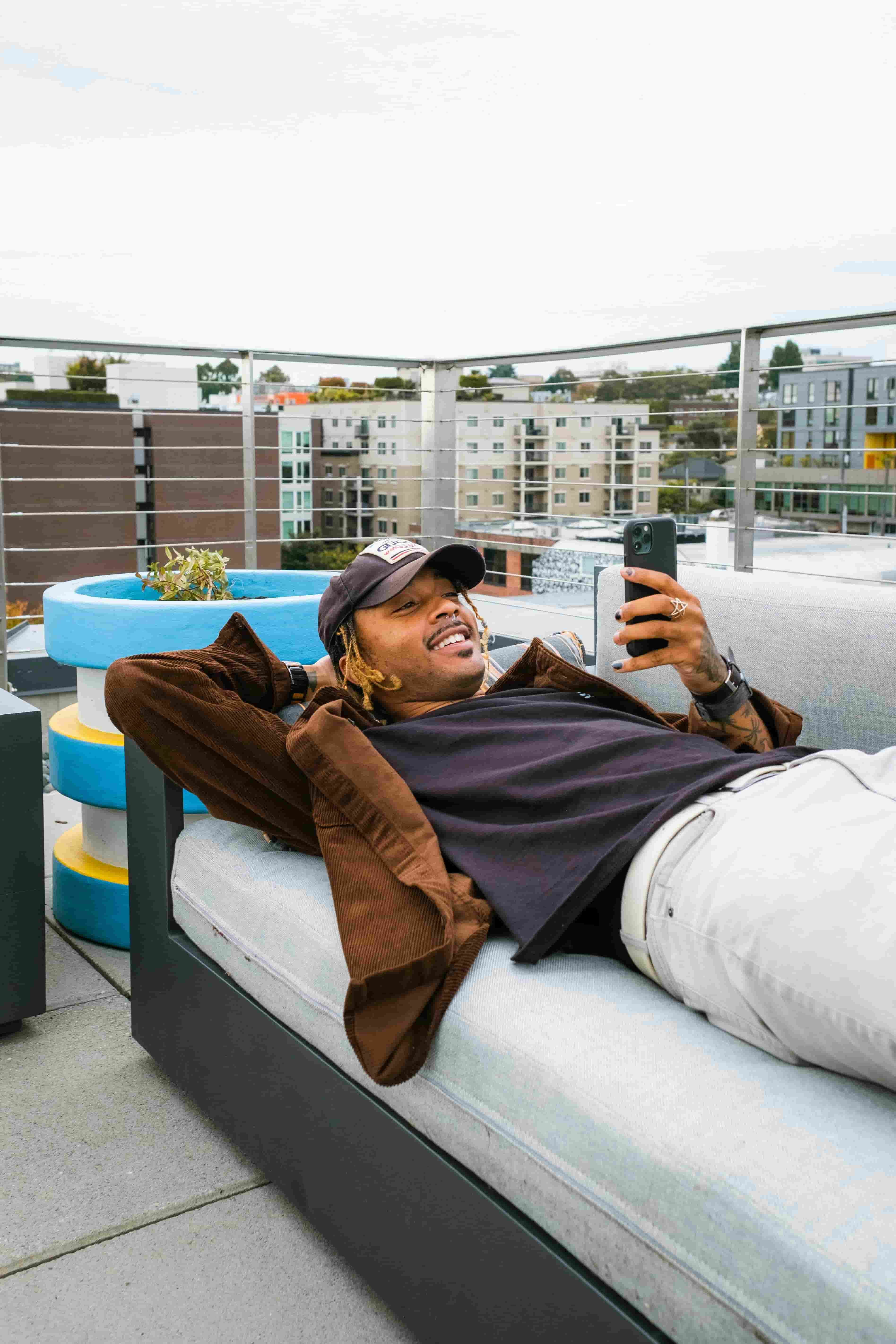 Man relaxing on a rooftop sofa, smiling at his phone