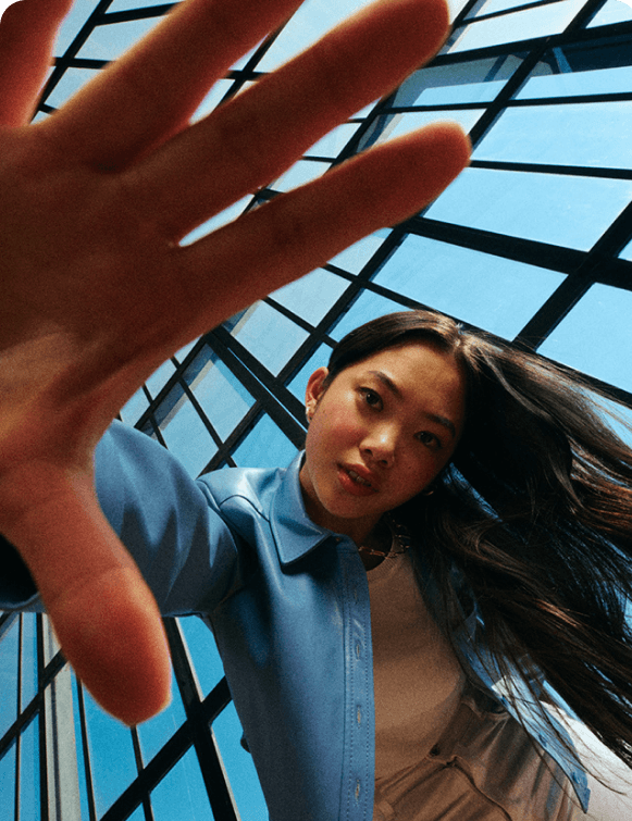 Woman reaching a hand toward the camera under a glass atrium roof