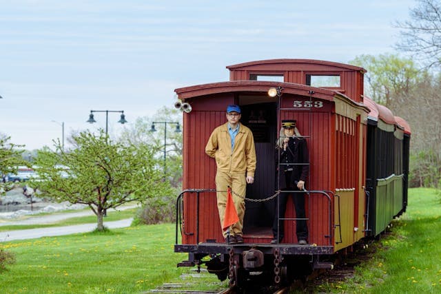 Vintage red caboose train car on tracks in a green rural landscape.