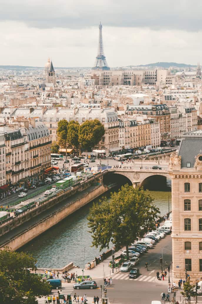 Aerial view of Paris featuring the Eiffel Tower, a bridge over the River Seine, and historic buildings under a cloudy sky.